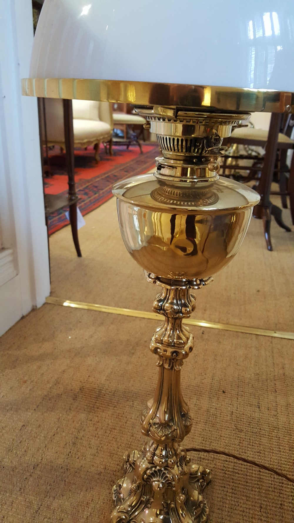 A Victorian brass oil lamp featuring a decorative cast base, fluted stem, central brass reservoir, and a white glass shade. View V