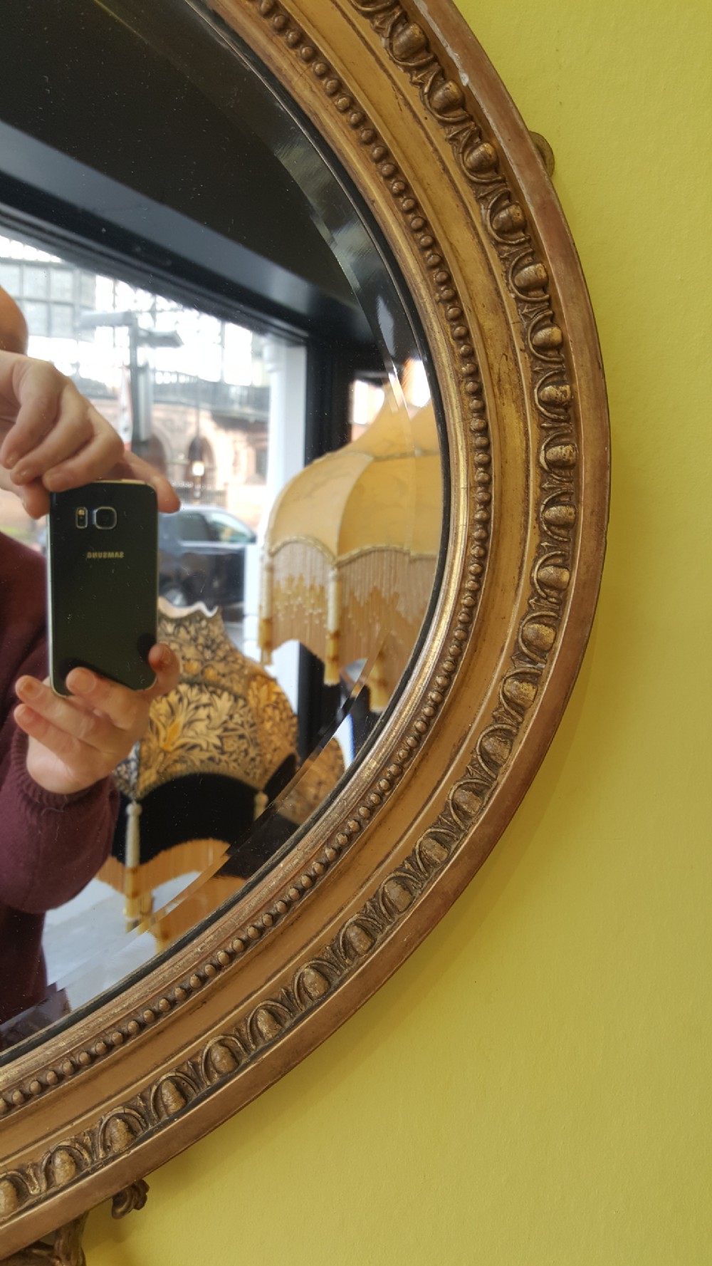 An oval Adam Revival giltwood mirror featuring a top crest with a classical urn, scrolling foliate detail, and a carved shell motif at the base. View III