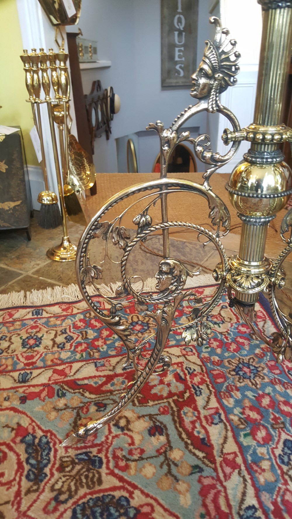 An early 20th-century brass standard lamp featuring an ornate scrollwork tripod base and a botanical patterned domed shade with cream textile fringing. View II