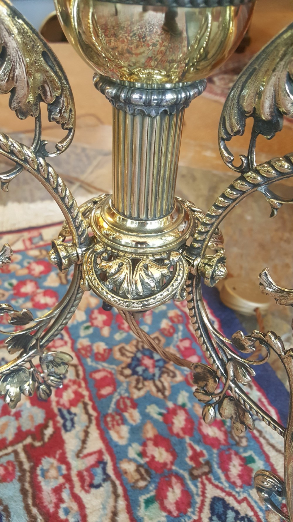 An early 20th-century brass standard lamp featuring an ornate scrollwork tripod base and a botanical patterned domed shade with cream textile fringing. View V