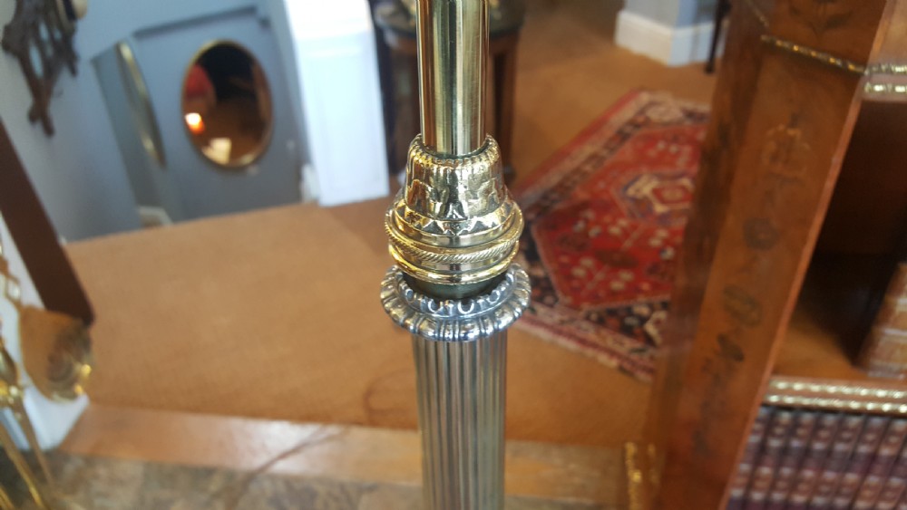 An early 20th-century brass standard lamp featuring an ornate scrollwork tripod base and a botanical patterned domed shade with cream textile fringing. View VI