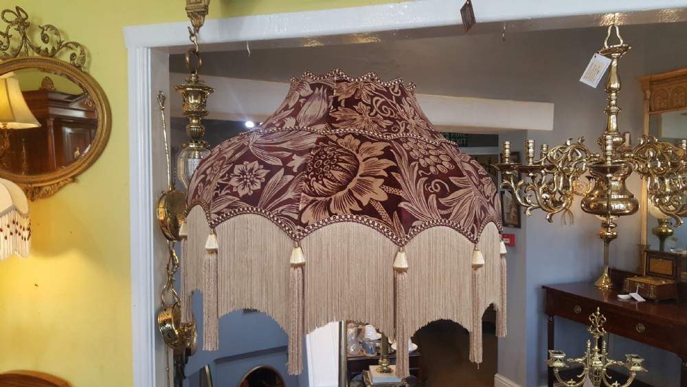 An early 20th-century brass standard lamp featuring an ornate scrollwork tripod base and a botanical patterned domed shade with cream textile fringing. View VIII