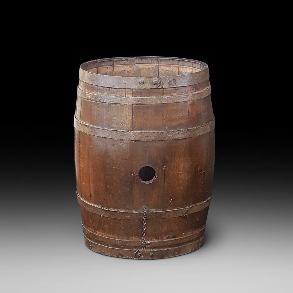 An early twentieth-century coopered oak barrel bound with dark iron hoops and featuring a central bung hole.