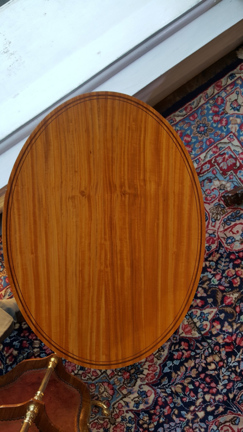 An Edwardian oval satinwood occasional table featuring slender square tapered legs, crossbanded inlay along the top edge, and a small oval lower undertier. View II