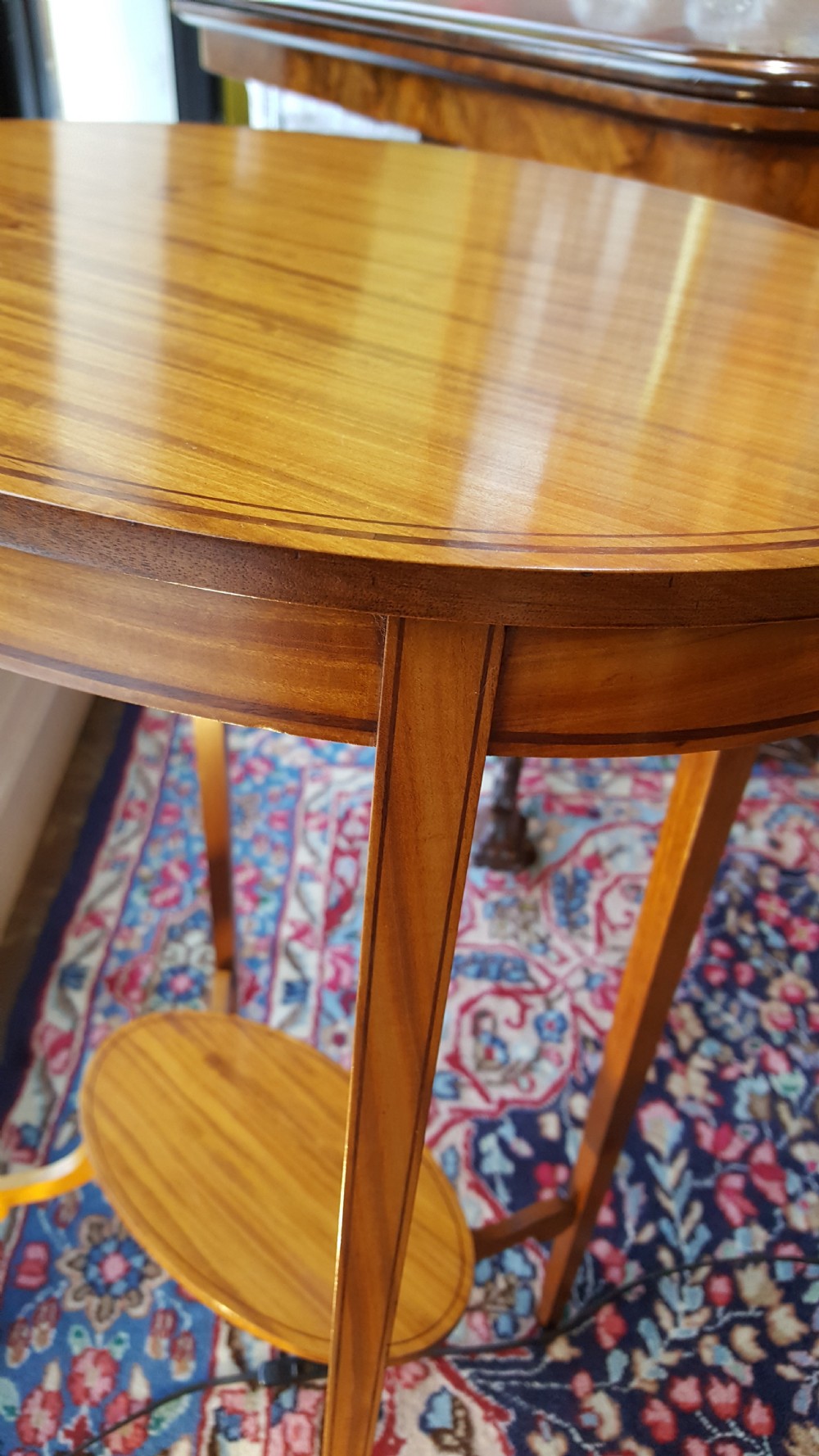 An Edwardian oval satinwood occasional table featuring slender square tapered legs, crossbanded inlay along the top edge, and a small oval lower undertier. View V