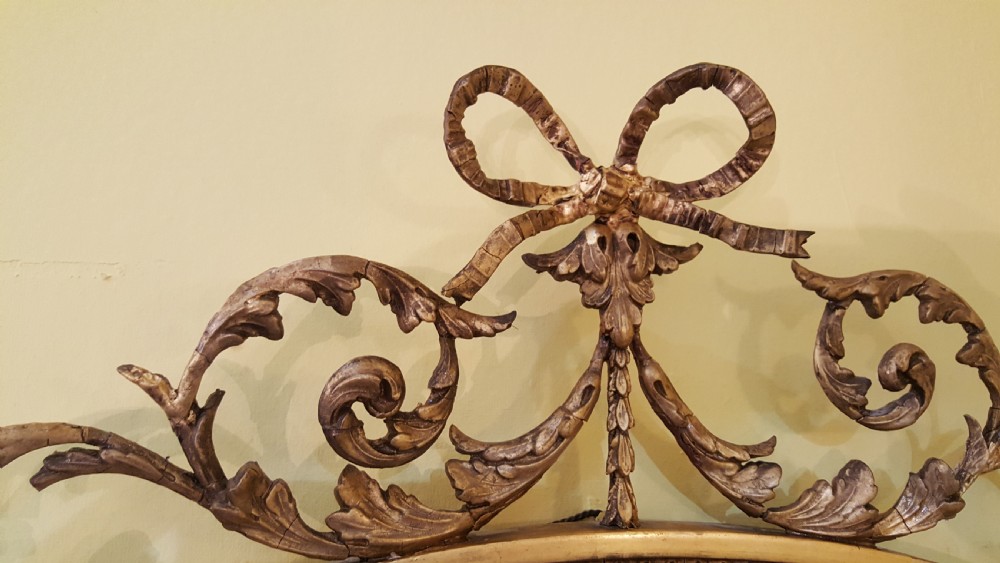 An oval Adam Revival wall mirror featuring a gilt and gesso frame adorned with a ribbon knot cresting and foliate swags. View III