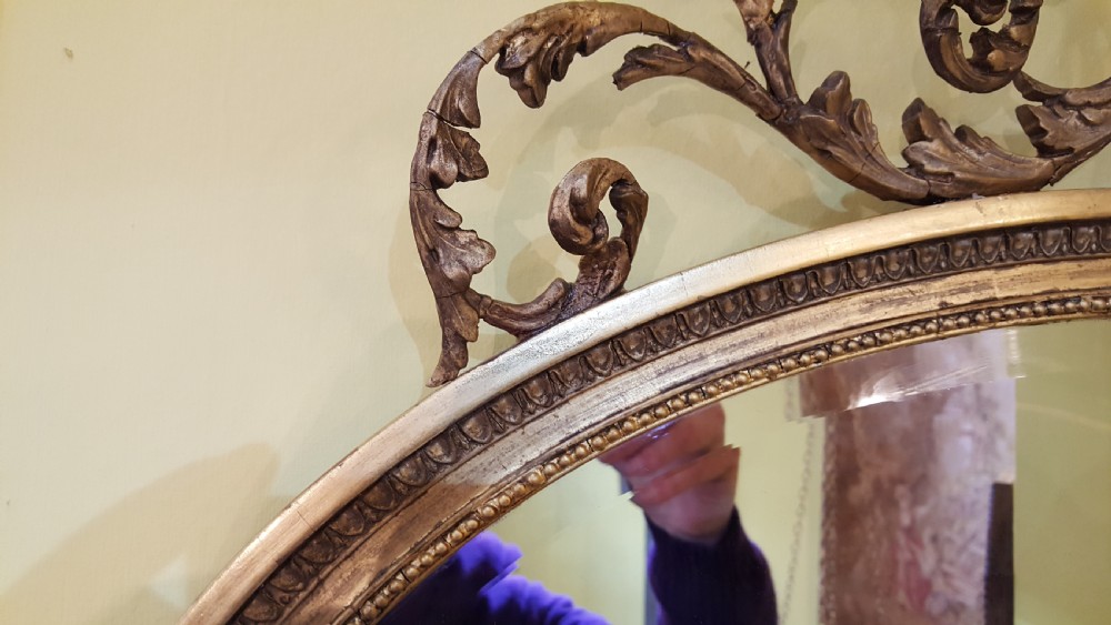 An oval Adam Revival wall mirror featuring a gilt and gesso frame adorned with a ribbon knot cresting and foliate swags. View IV
