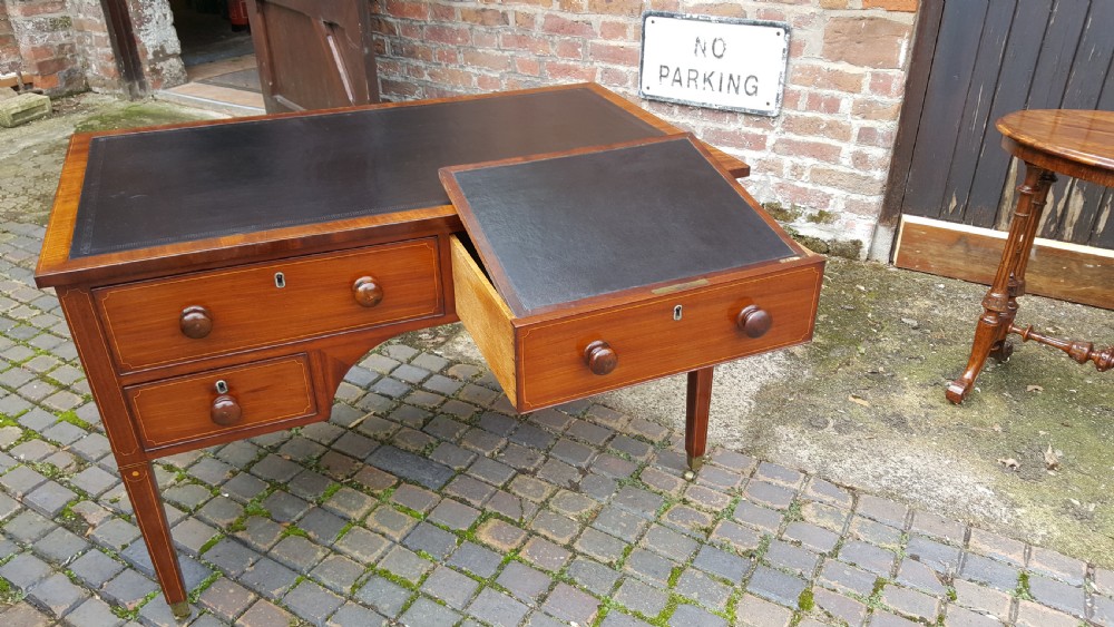 A George III mahogany writing desk featuring a black leather inset top, four drawers with turned wooden knobs, boxwood stringing inlay, an arched central apron, and square tapered legs on brass castors. View VIII