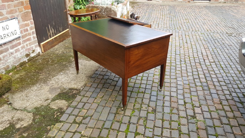 A George III mahogany writing desk featuring a black leather inset top, four drawers with turned wooden knobs, boxwood stringing inlay, an arched central apron, and square tapered legs on brass castors. View IX