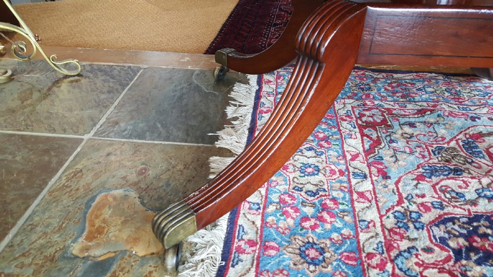 A Regency period rectangular mahogany tilt-top table with crossbanded edges supported by a central turned column and four reeded splayed legs on brass castors. View II
