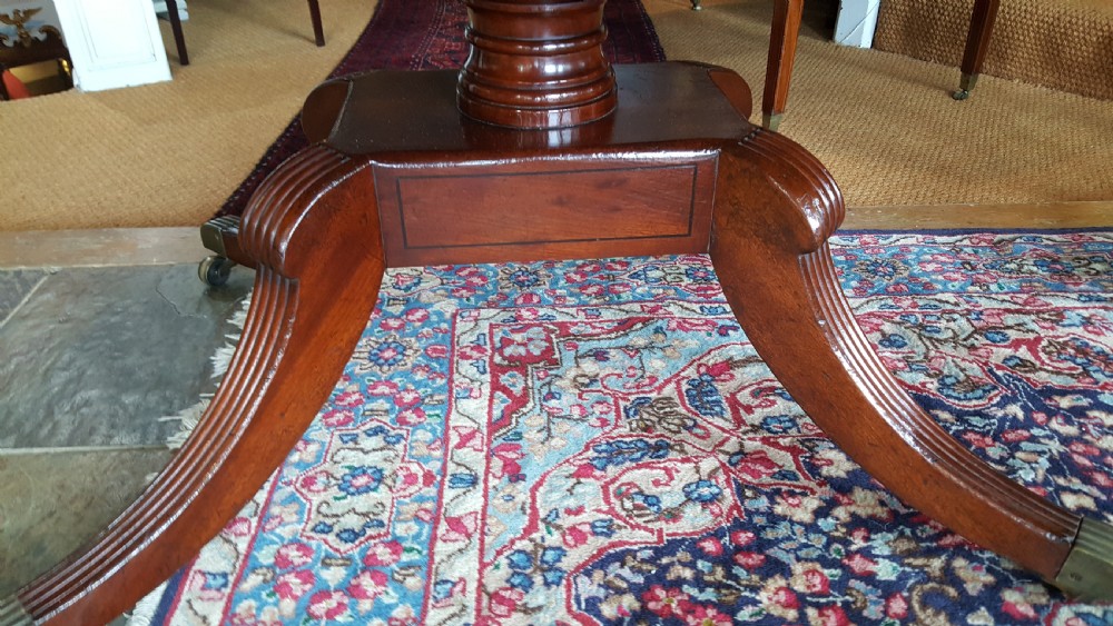 A Regency period rectangular mahogany tilt-top table with crossbanded edges supported by a central turned column and four reeded splayed legs on brass castors. View III