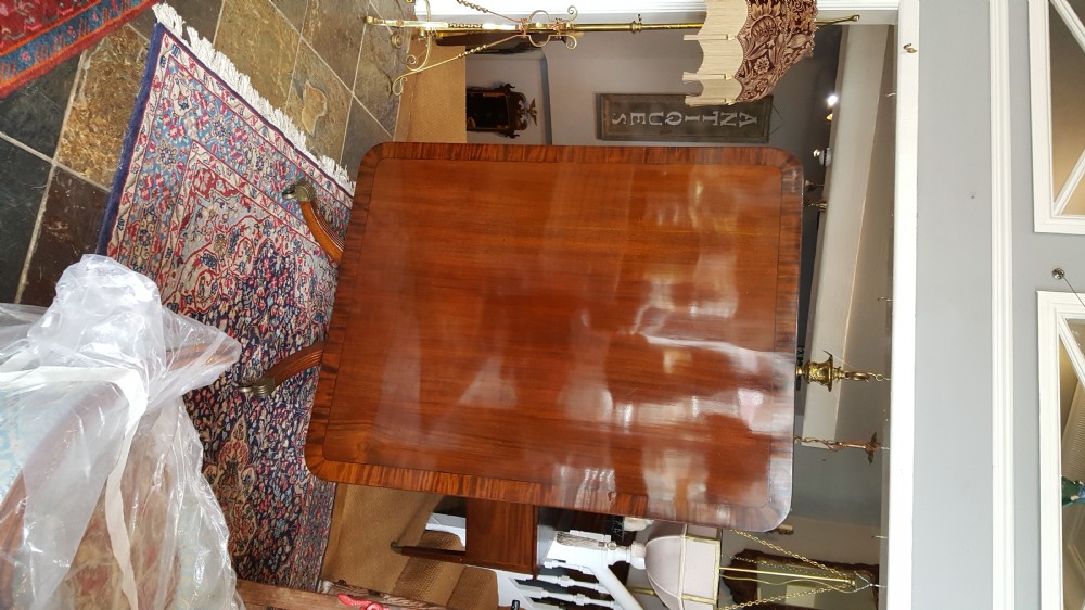 A Regency period rectangular mahogany tilt-top table with crossbanded edges supported by a central turned column and four reeded splayed legs on brass castors. View VII