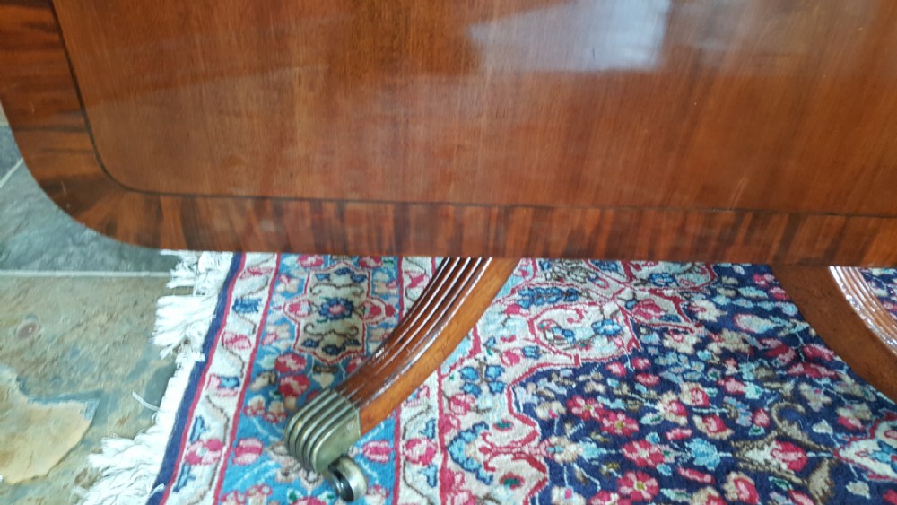 A Regency period rectangular mahogany tilt-top table with crossbanded edges supported by a central turned column and four reeded splayed legs on brass castors. View VIII