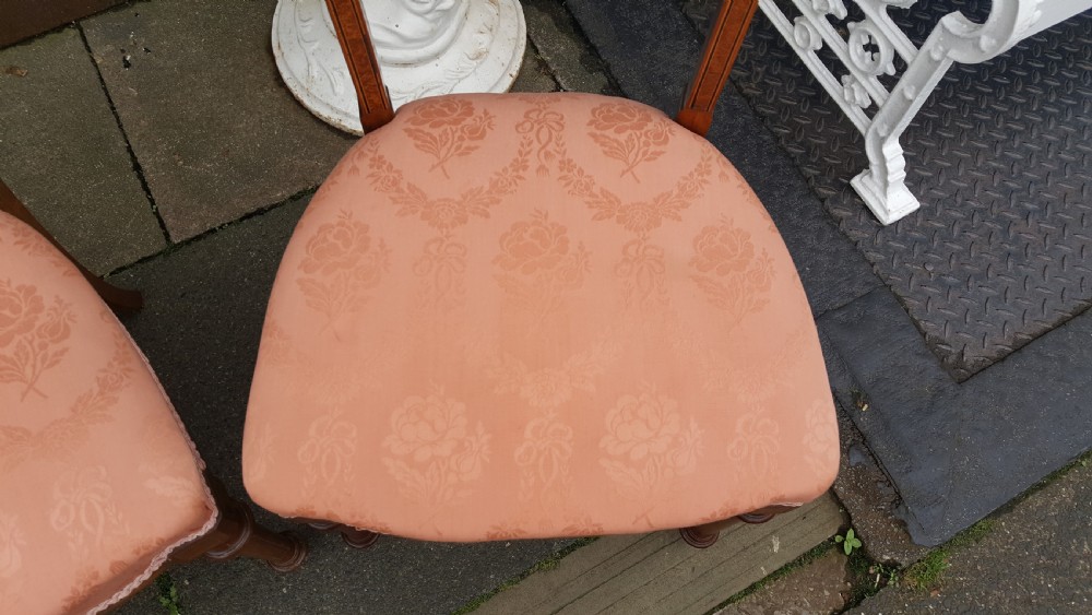 A set of four Victorian walnut salon chairs featuring carved rectangular open backs, turned front legs, and seats upholstered in dusty pink damask with braid trim. View V