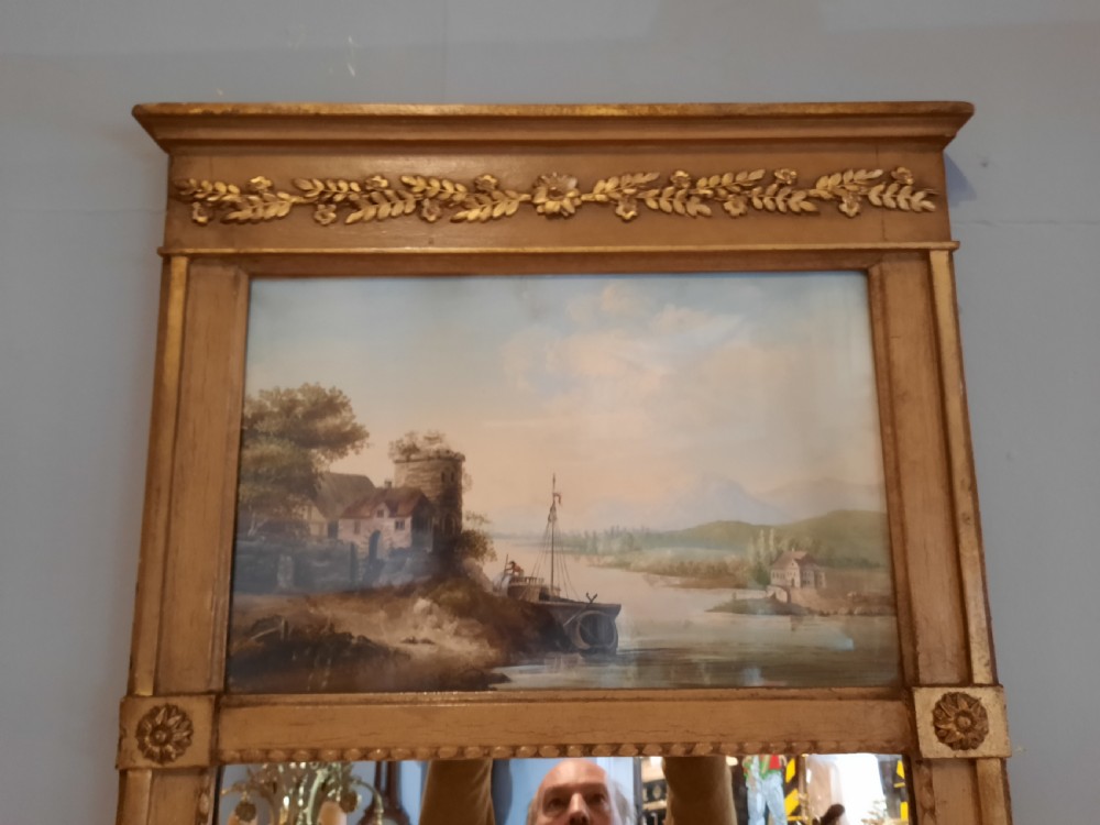 A tall 19th-century gilded composition trumeau mirror featuring an oil landscape painting set within the upper panel and a rectangular mirror plate below. View II