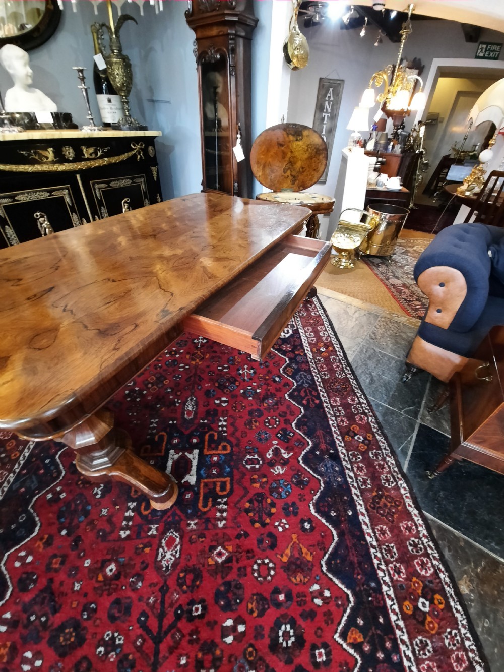 A Late Regency rosewood library table featuring a polished rectangular top with rounded corners, supported by dual faceted end supports resting on stepped plinth bases. View VI