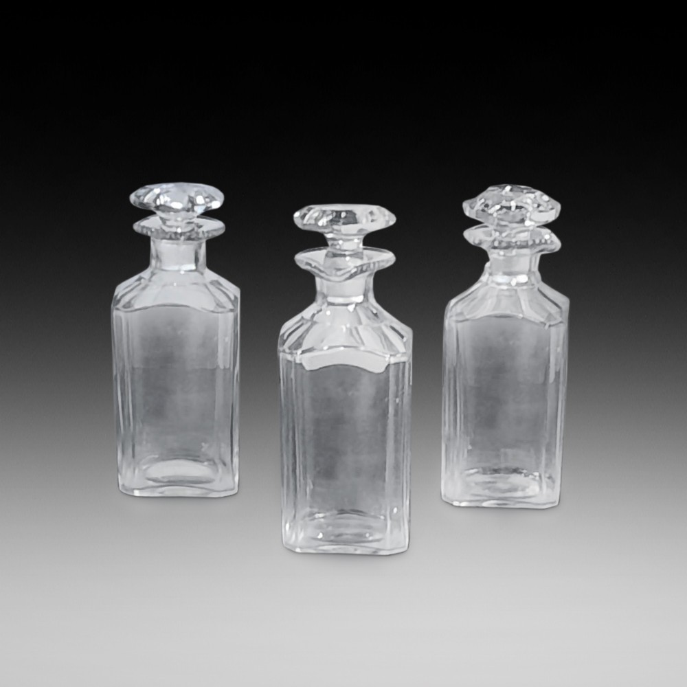 A set of three clear cut glass decanters from the William IV period featuring square bodies and faceted glass stoppers.