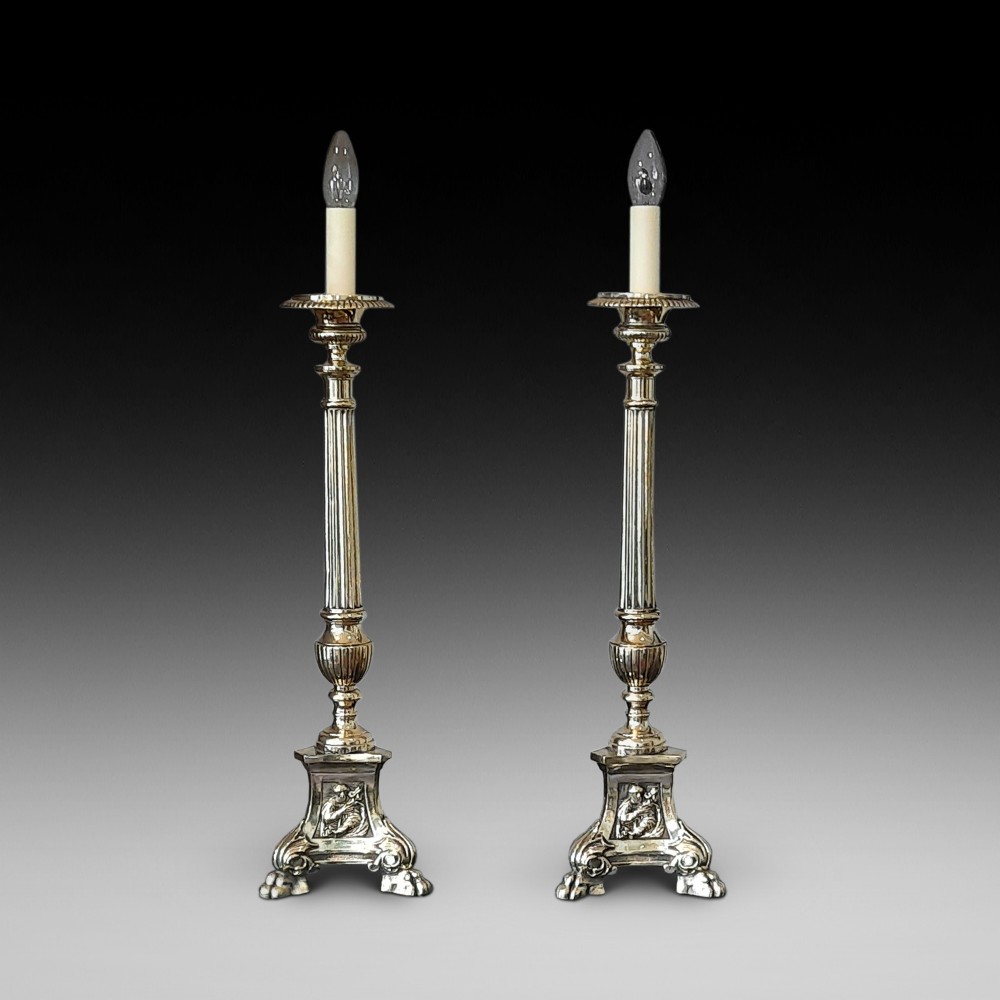 A matching pair of tall silver-plated table lamps styled as pricket candlesticks with fluted column shafts and decorated triform bases.