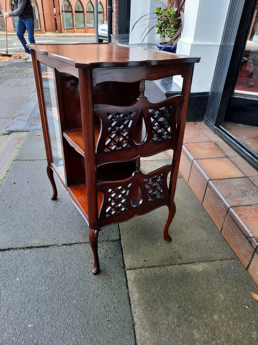 An Edwardian mahogany display table featuring a single-door glazed cabinet on the left and open two-tier shelving with pierced fretwork on the right, supported by cabriole legs. View IV