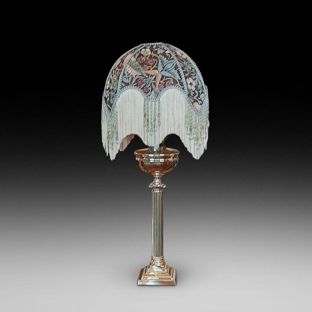A nineteenth-century brass table lamp featuring a fluted column support, square stepped base, and a decorated fabric shade with hanging fringe.