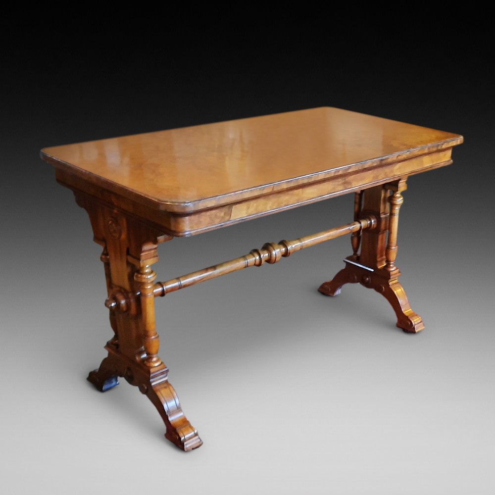 A Victorian walnut centre sofa table featuring a rectangular figured veneer top, turned stretcher, carved end supports, and dual feet.