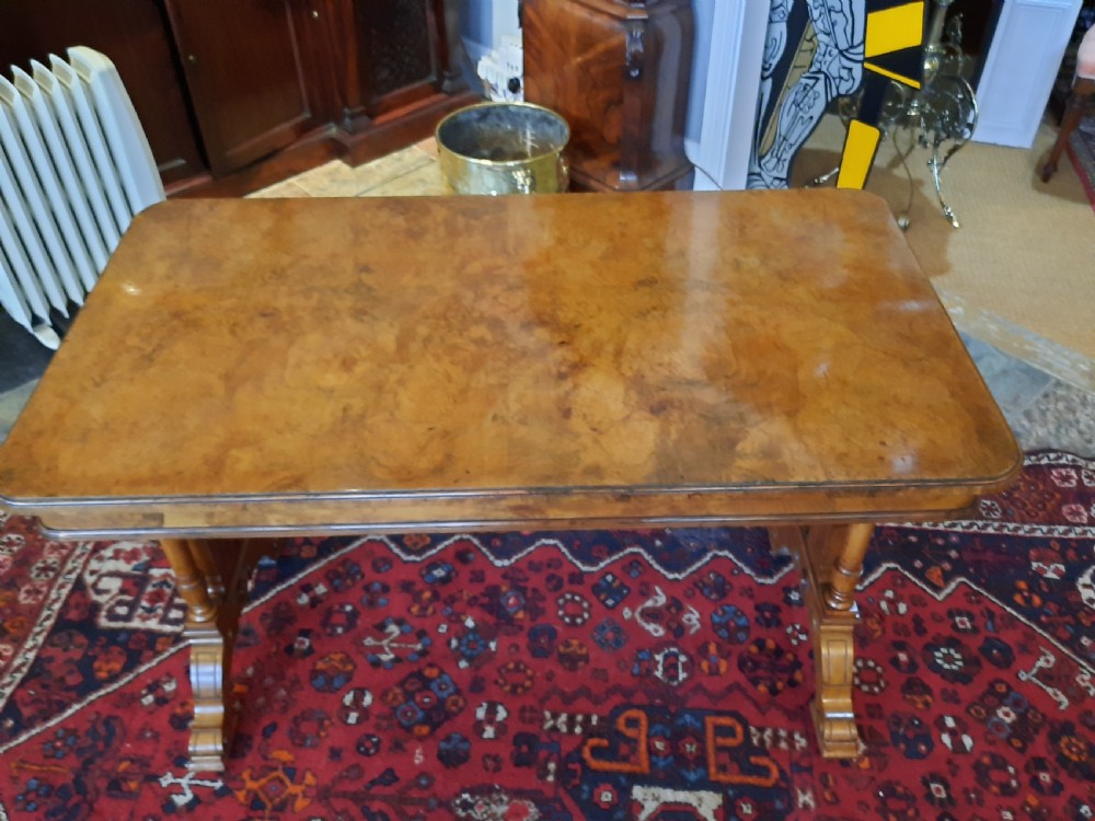 A Victorian walnut centre sofa table featuring a rectangular figured veneer top, turned stretcher, carved end supports, and dual feet. View VI