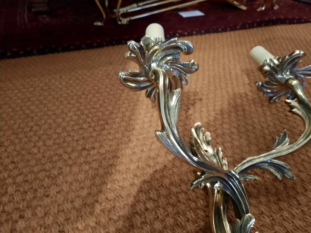 A cast brass twin-arm wall light in the Rococo Revival style featuring scrolling acanthus foliage and white faux candle sockets. View V