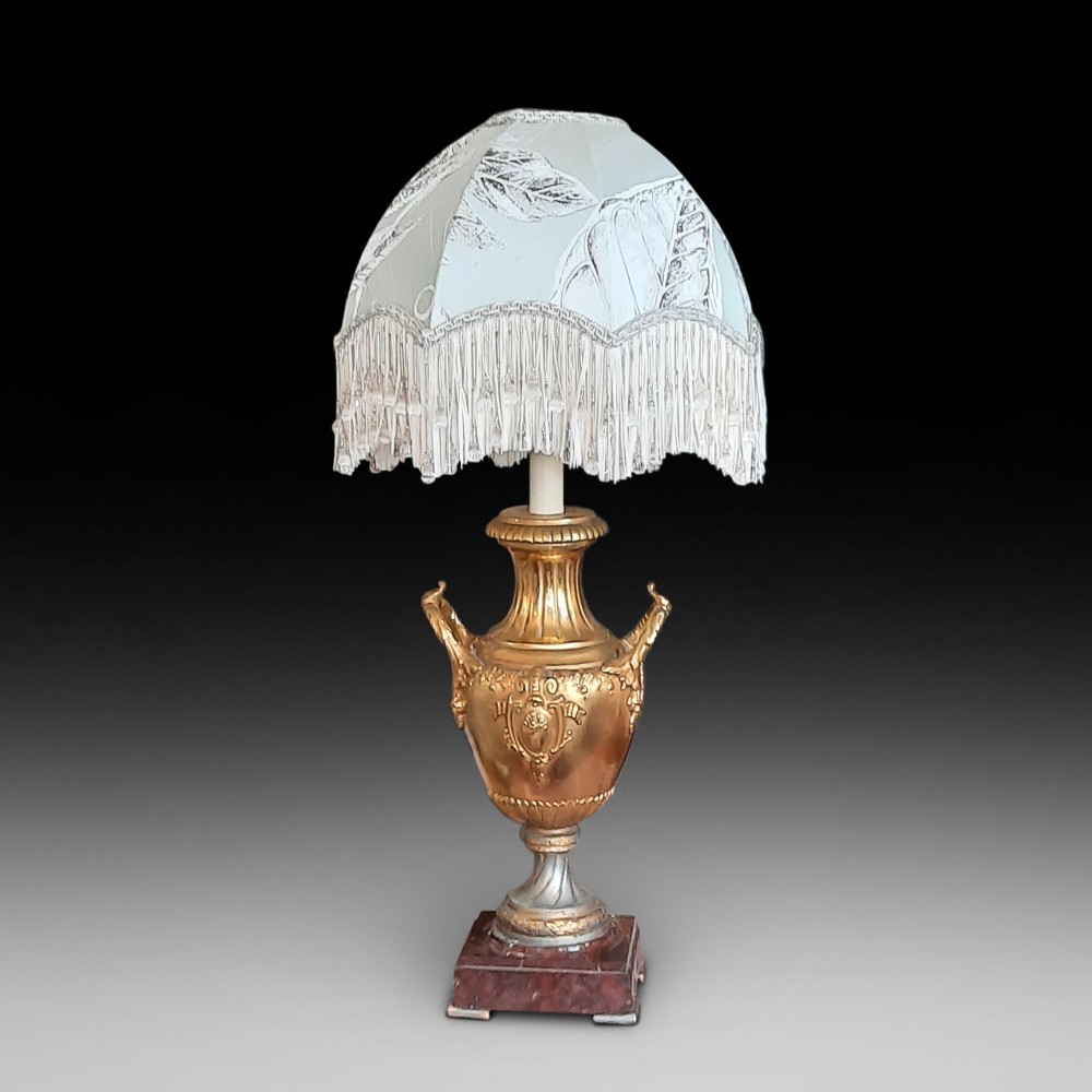A 19th-century gilt bronze classical urn mounted as a table lamp on a square marble base with a fringed fabric shade.