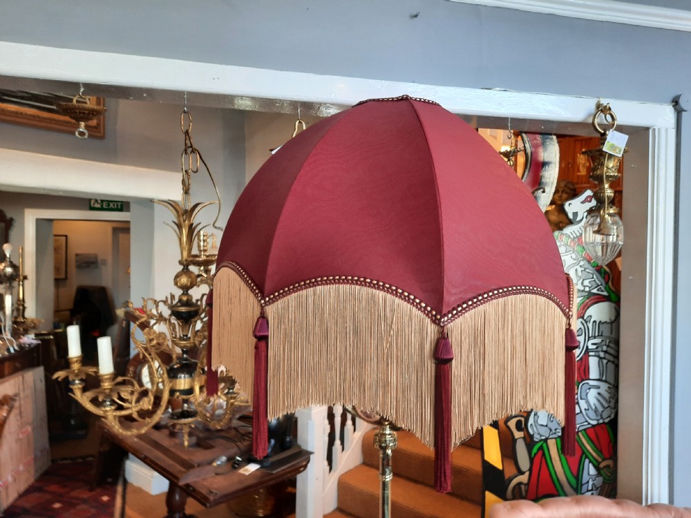 An antique Arts and Crafts adjustable brass floor lamp featuring a tripod base, twisted support column, and a dome-shaped red fabric shade with tassel fringe. View II