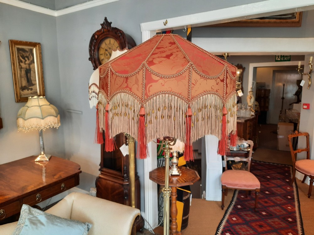 An early 20th-century Art Nouveau brass standard lamp featuring openwork base detailing and a patterned terracotta lampshade with fringe and tassels. View VI