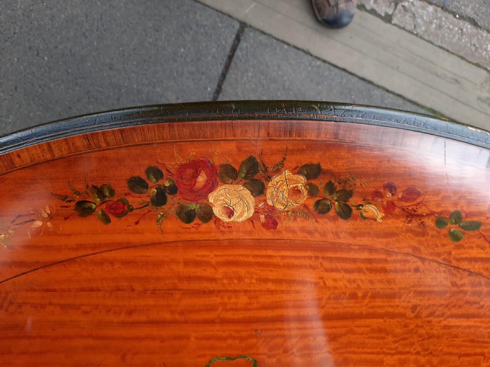 An Edwardian oval satinwood occasional table featuring hand-painted floral decoration on the top, slender tapered legs, and an X-form stretcher with a central wooden urn finial. View V