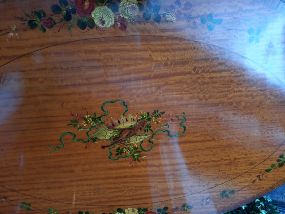 An Edwardian oval satinwood occasional table featuring hand-painted floral decoration on the top, slender tapered legs, and an X-form stretcher with a central wooden urn finial. View VI