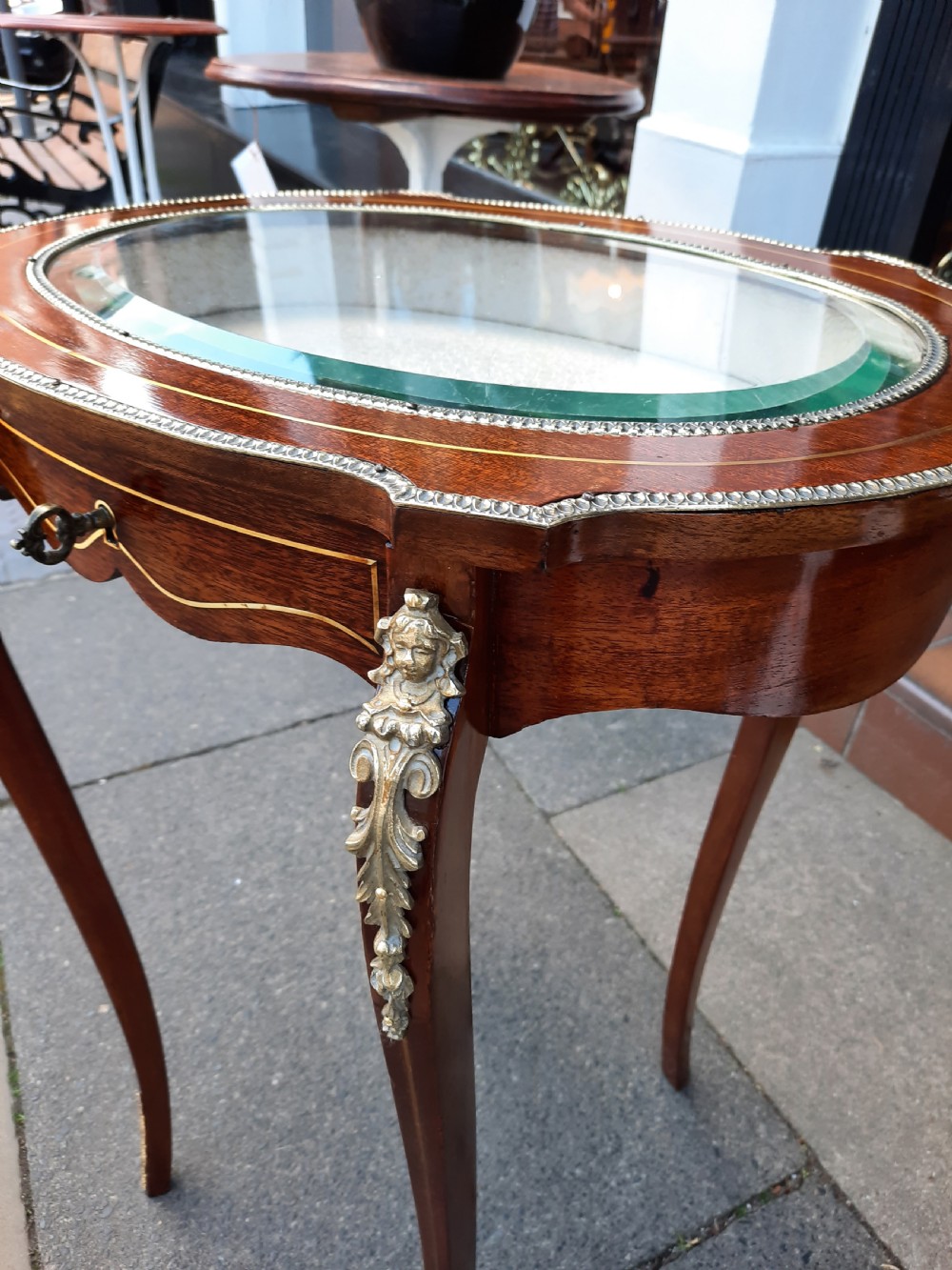 A late 19th-century French mahogany bijouterie table featuring an oval glass-inset top, slender cabriole legs, and ornate metal mounts. View IV