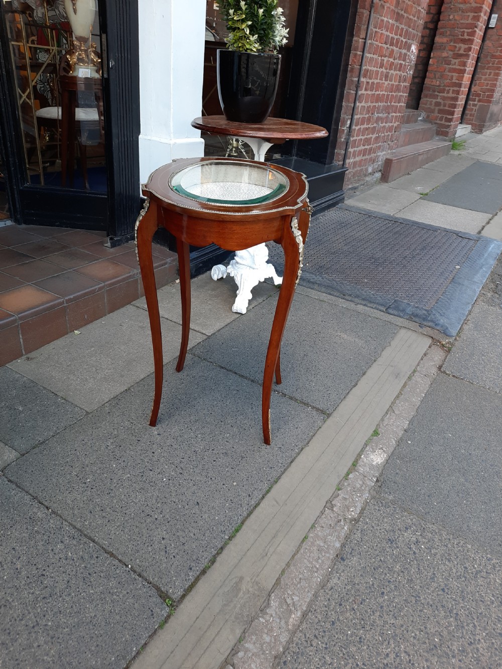 A late 19th-century French mahogany bijouterie table featuring an oval glass-inset top, slender cabriole legs, and ornate metal mounts. View V