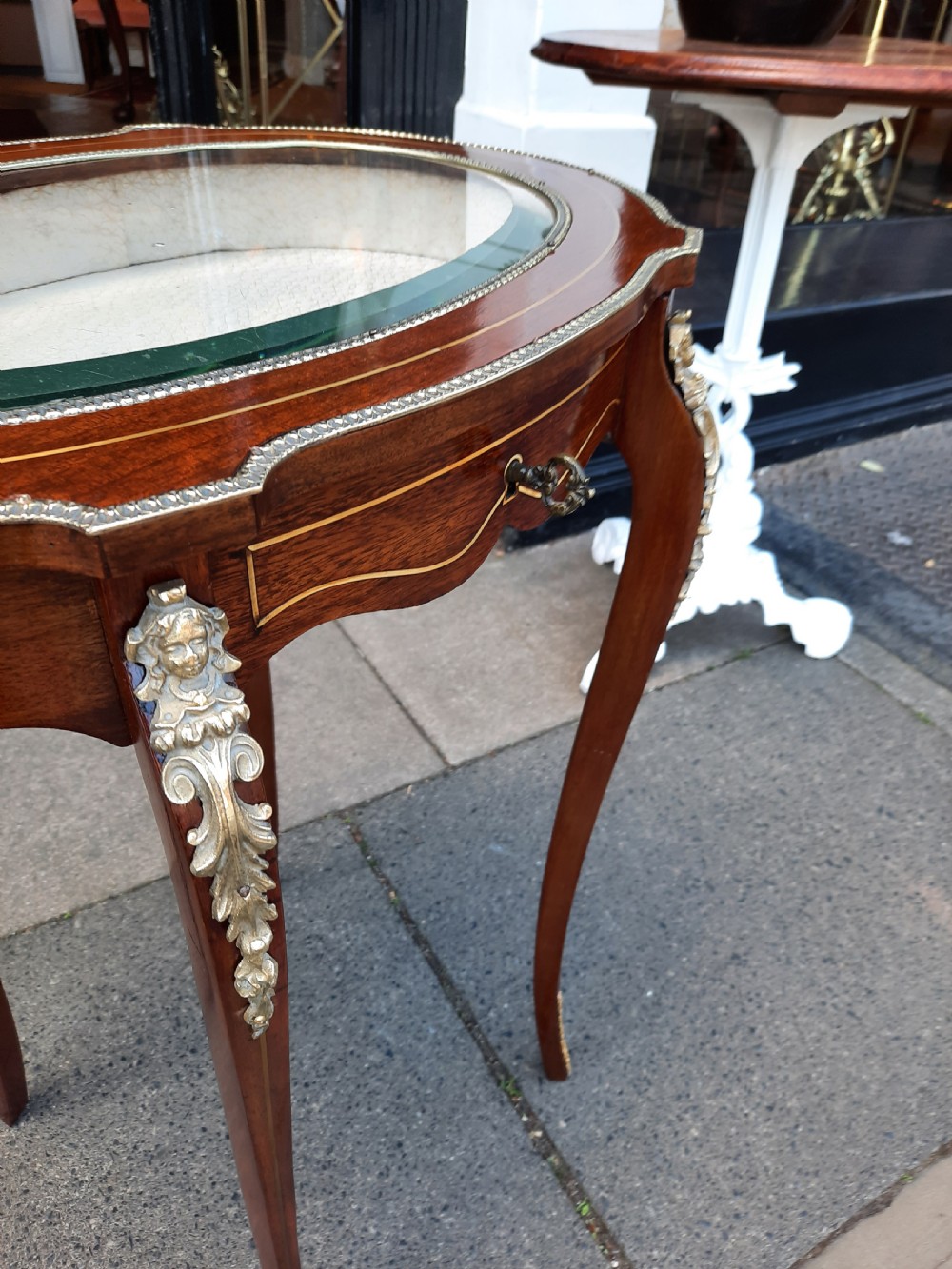 A late 19th-century French mahogany bijouterie table featuring an oval glass-inset top, slender cabriole legs, and ornate metal mounts. View VI