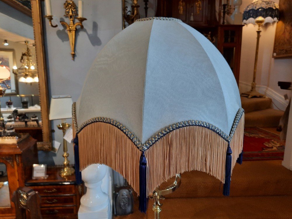 An Arts and Crafts style brass standard lamp featuring a scrolled tripod base, adjustable telescopic shaft, and a domed blue fabric shade with tassel fringe. View II