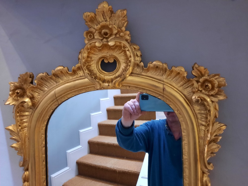 A tall arched late Victorian pier mirror featuring an ornate gold giltwood frame with carved foliate scrolls and a top cresting finial. View V
