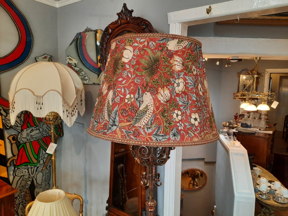 An Arts and Crafts copper floor lamp featuring an adjustable central stem, scrollwork base, and a patterned fabric shade. View V