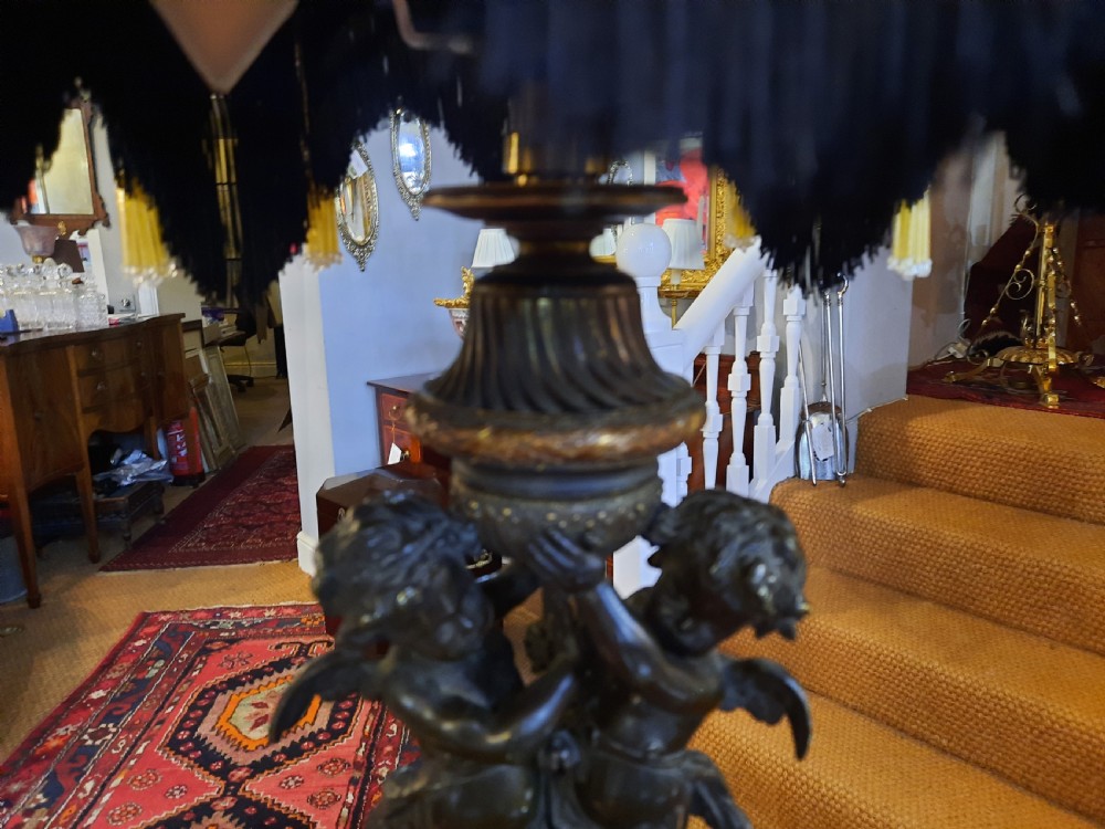 An antique French bronze table lamp with sculpted cherub figures resting on a marble base, topped with a cream and black scalloped fabric shade. View IV