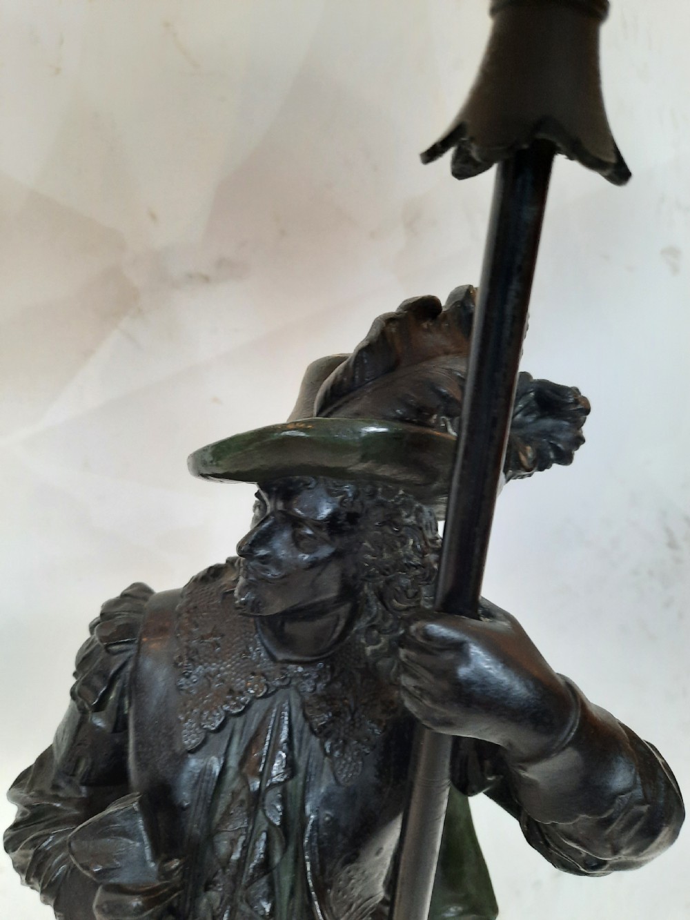 A pair of late nineteenth-century dark spelter table lamps featuring detailed cast musketeer figures supporting pike shafts fitted with cream shades. View V