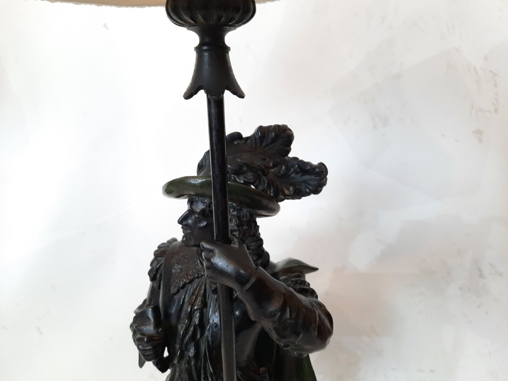 A pair of late nineteenth-century dark spelter table lamps featuring detailed cast musketeer figures supporting pike shafts fitted with cream shades. View VI