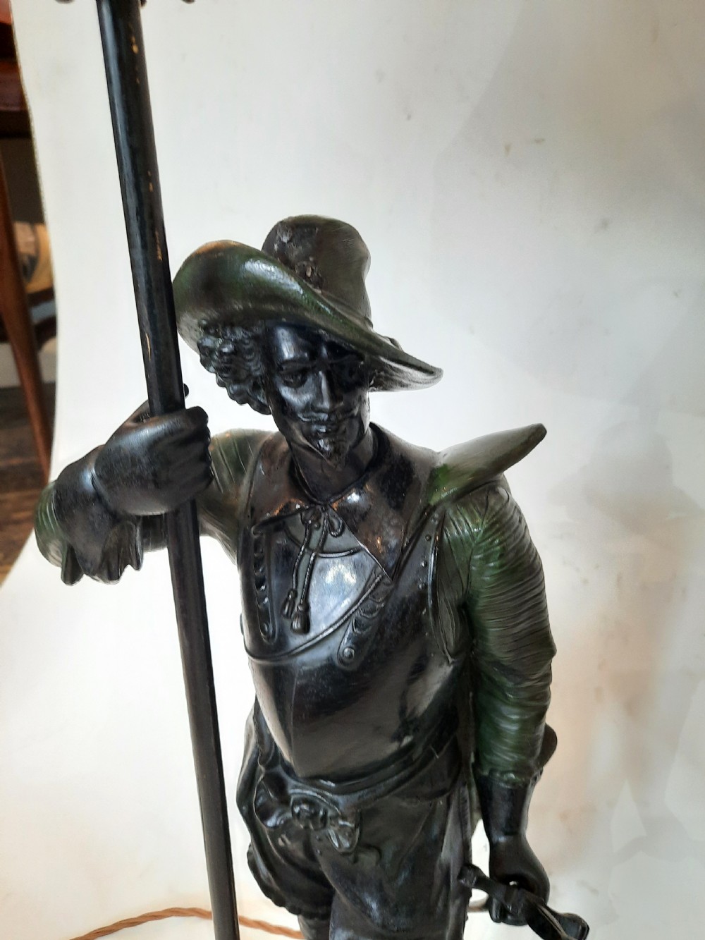 A pair of late nineteenth-century dark spelter table lamps featuring detailed cast musketeer figures supporting pike shafts fitted with cream shades. View IX