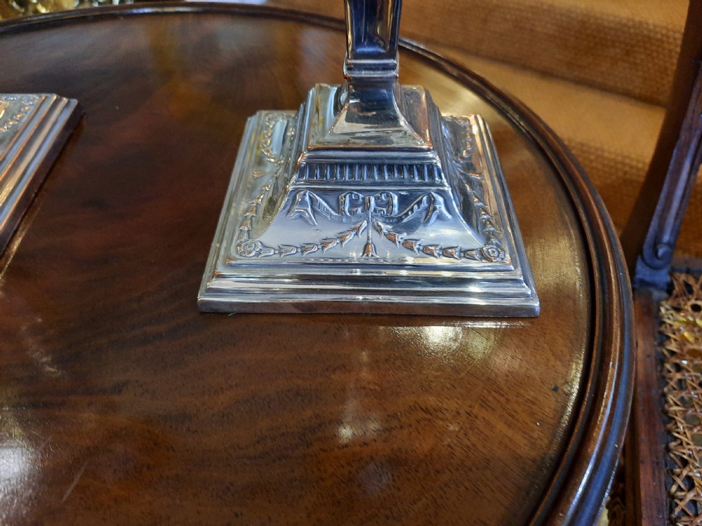 A pair of silver-plated candlesticks designed in the Adam Revival style, showcasing tapered column shafts with swag relief details on stepped square bases. View II