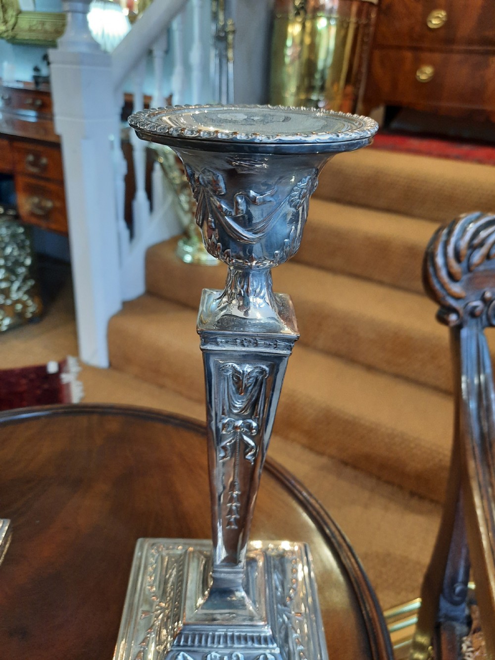 A pair of silver-plated candlesticks designed in the Adam Revival style, showcasing tapered column shafts with swag relief details on stepped square bases. View III
