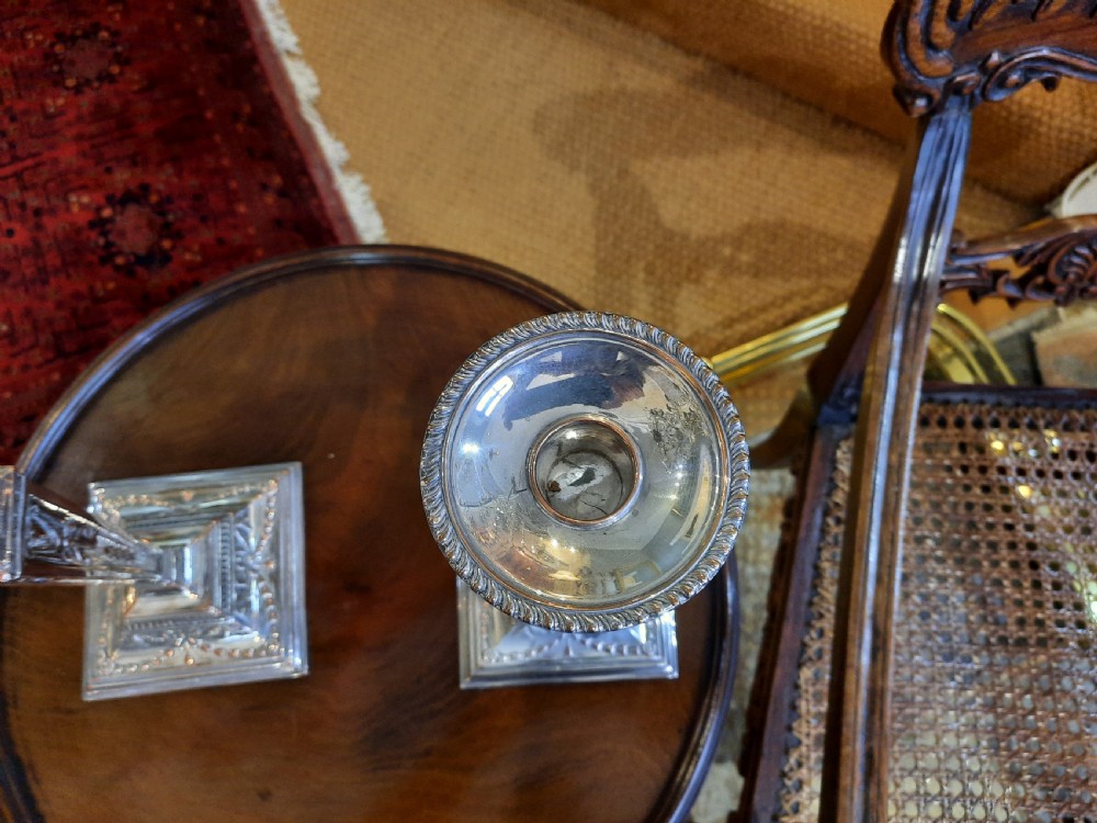 A pair of silver-plated candlesticks designed in the Adam Revival style, showcasing tapered column shafts with swag relief details on stepped square bases. View IV