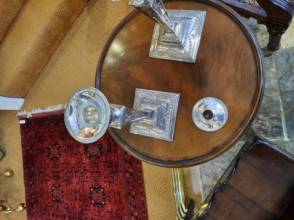A pair of silver-plated candlesticks designed in the Adam Revival style, showcasing tapered column shafts with swag relief details on stepped square bases. View V