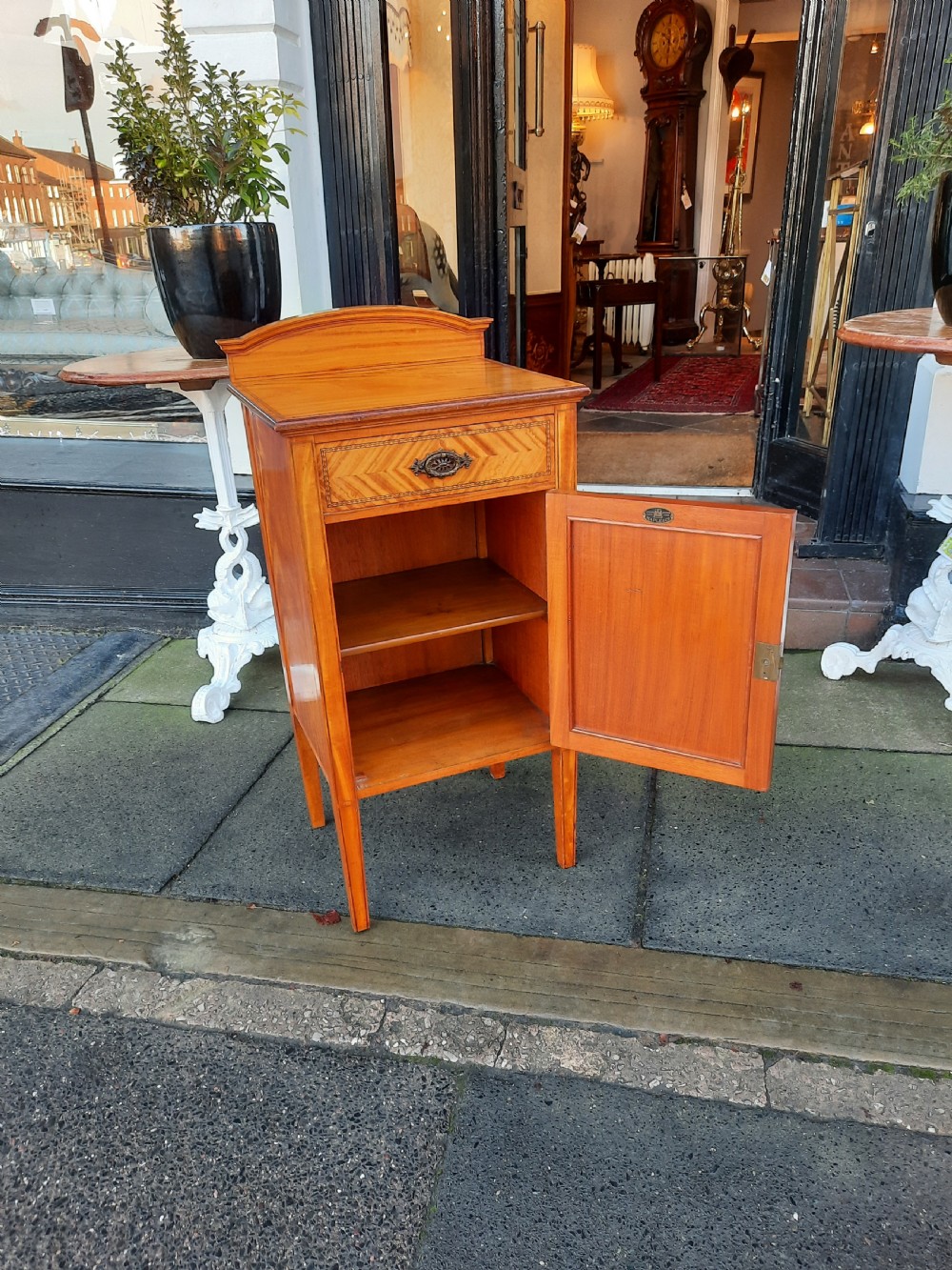 An Edwardian satinwood bedside cabinet featuring chevron pattern veneered door and drawer panels, metal drop handles, and tapered square legs. View VII