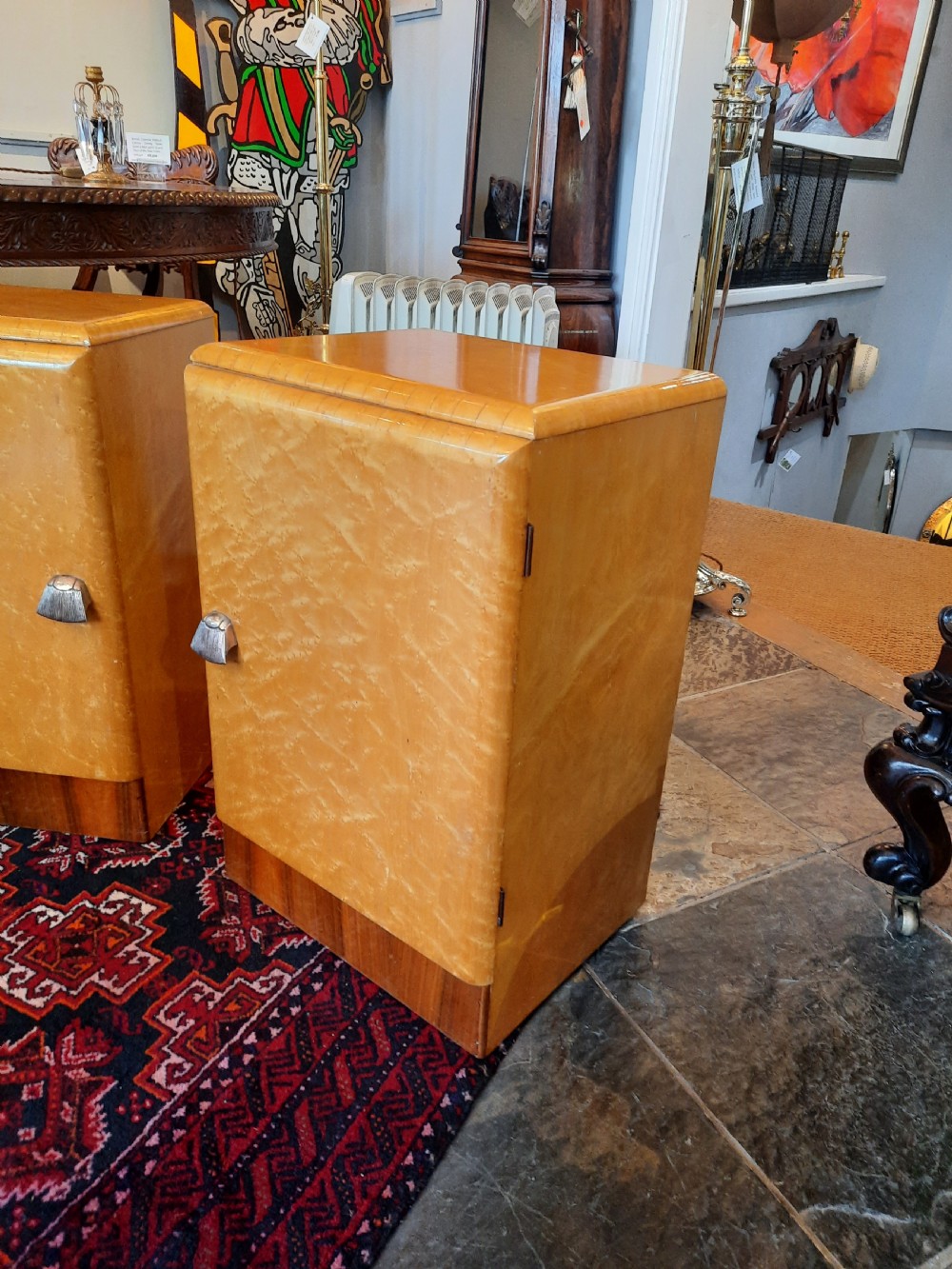A pair of Art Deco bedside cabinets featuring golden parchment door fronts, contrast dark wood plinths, and small metal handles. View V