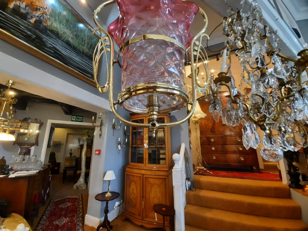 An Art Nouveau brass pendant light frame housing a ruffled cranberry glass shade with a moulded diamond pattern. View V