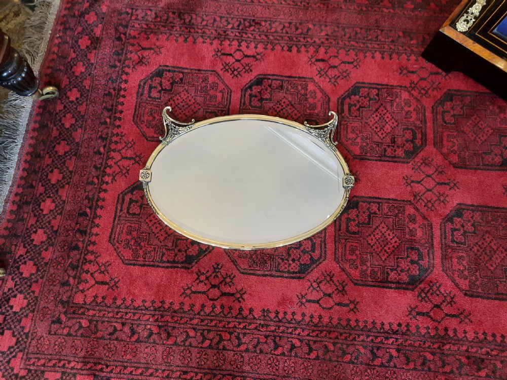 A late 19th-century oval mirror featuring a polished brass frame with decorative scrolled cresting and rosette side accents. View II